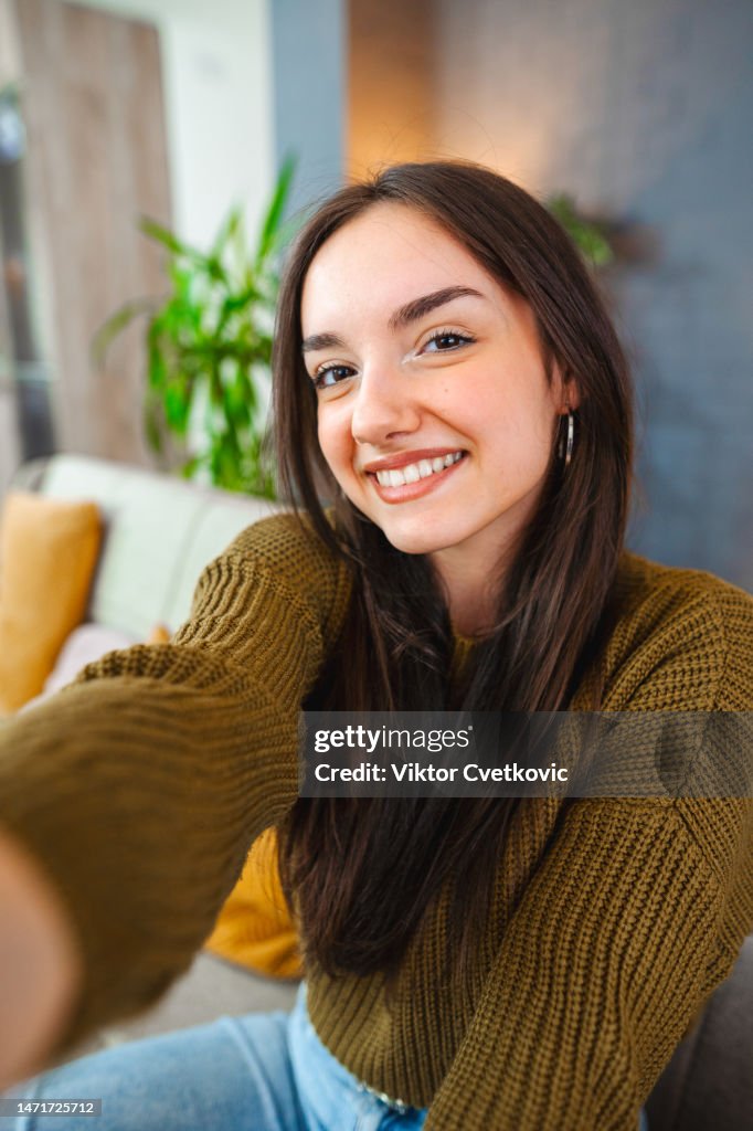 Smiling young woman taking selfies while relaxing at home