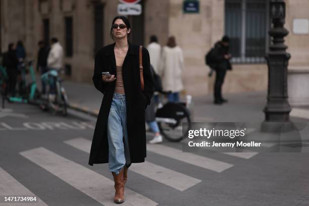 Fashion week guest seen wearing Yves Saint Laurent shades, a black coat, oversized jeans, brown leather cowboy boots, a beige shirt and a brown bag...