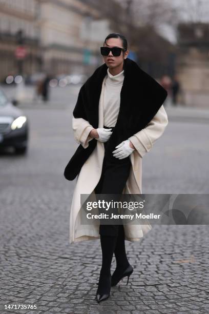 Fashion week guest seen wearing a black and white look with black shades, a white coat with a black collar, white gloves, a black skirt, black tights...