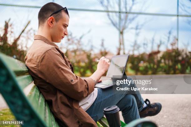 young man sitting on a park bench, using digital tablet and digital pen. - e learning draw stock pictures, royalty-free photos & images