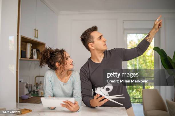 a young couple, a man and a woman, are setting up a security camera for home surveillance in their apartment - security camera house stock pictures, royalty-free photos & images