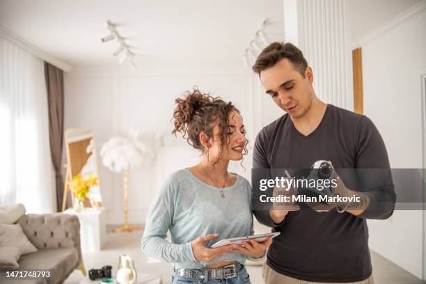 a young couple, a man and a woman, are setting up a security camera for home surveillance in their apartment - security camera house stock pictures, royalty-free photos & images