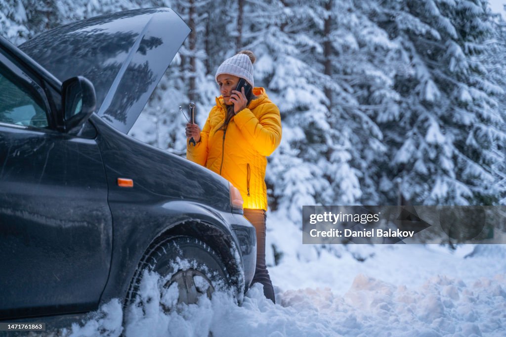 Winter car breakdown, woman calls for help.