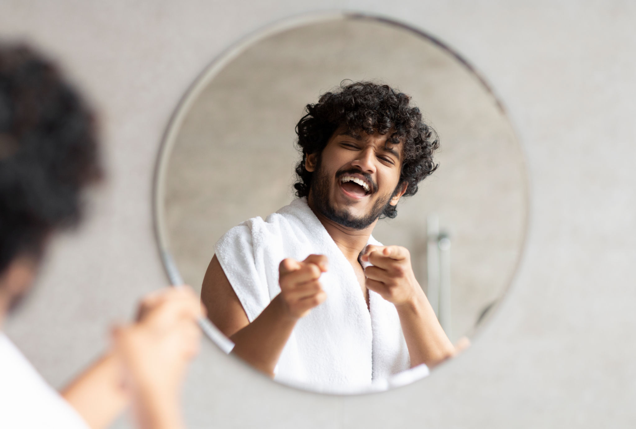 Excited indian guy pointing at mirror in bathroom with two fingers, standing with towel on shoulder Excited indian guy pointing at mirror in bathroom with two fingers, standing with towel on shoulder