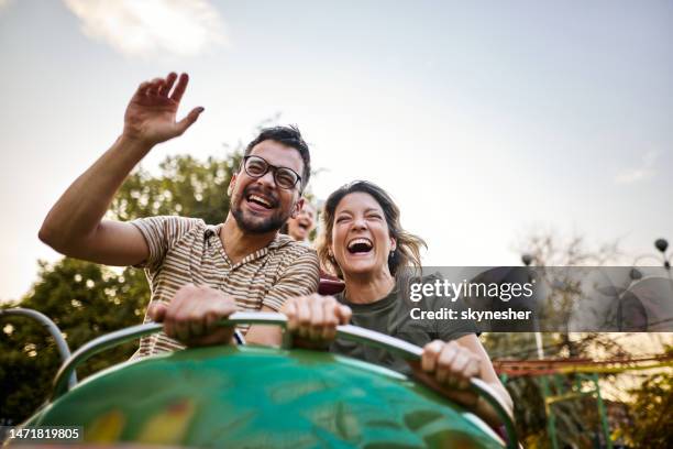 pareja despreocupada divirtiéndose en la montaña rusa en el parque de atracciones. - montaña rusa fotografías e imágenes de stock