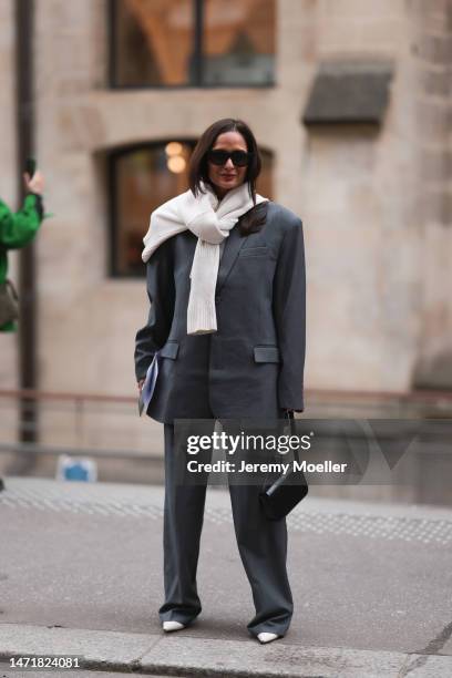 Fashion Week Guest is seen wearing a grey suit, blazer and wide pants, black leather handbag and white pullover and black sunglasses outside Lanvin...