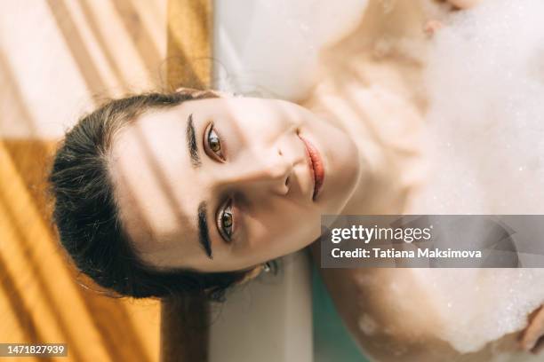 young woman relaxing in bath tub full of foam bubbles. self care and mental health concept. - woman bath bubbles stock-fotos und bilder