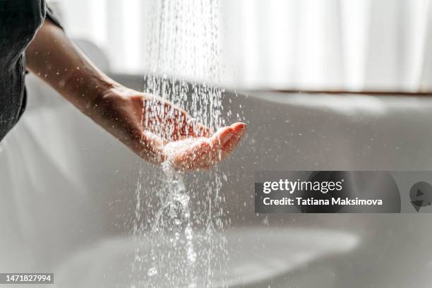 a woman's hand touches the water running from the shower. - lluvia fotografías e imágenes de stock