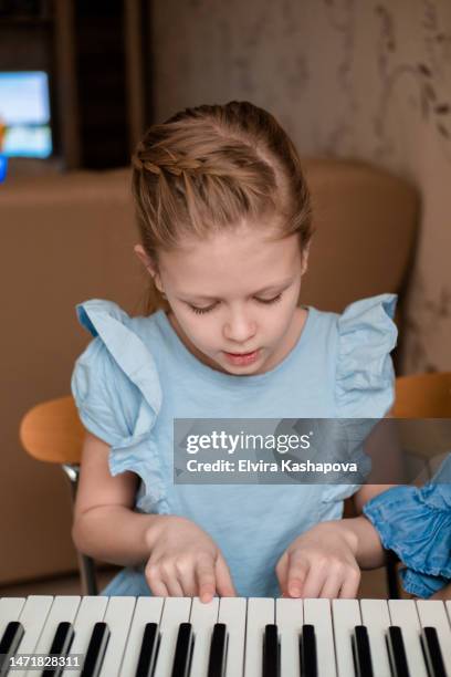 a girl with blond hair and in a denim dress learns to play the piano - child pianist stock pictures, royalty-free photos & images