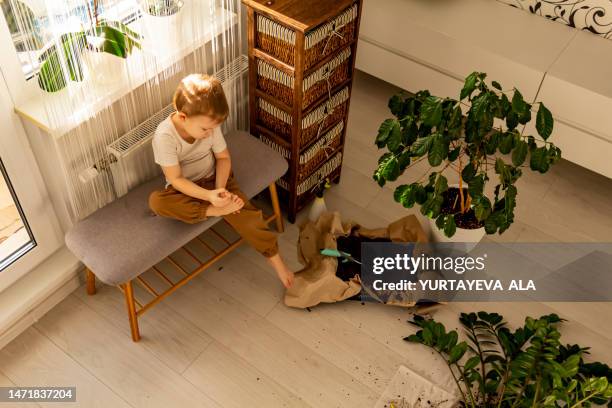 a small fair-haired child cleans his feet of debris in a room where there is a lot of mess and dirt. - fair haired boy stock-fotos und bilder