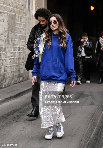Guest is seen wearing a blue hoodie, sequin skirt and cream sneakers outside the Rokh show during Paris Fashion Week F/W 2023 on March 06, 2023 in...
