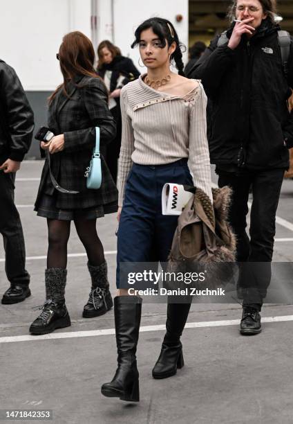 Guest is seen wearing a tan sweater, blue shorts, black boots and brown jacket outside the Rokh show during Paris Fashion Week F/W 2023 on March 06,...