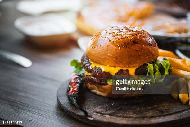 leckerer doppelburger mit pommes frites und gemüse auf holzschneidebrett - cheeseburger and fries stock-fotos und bilder