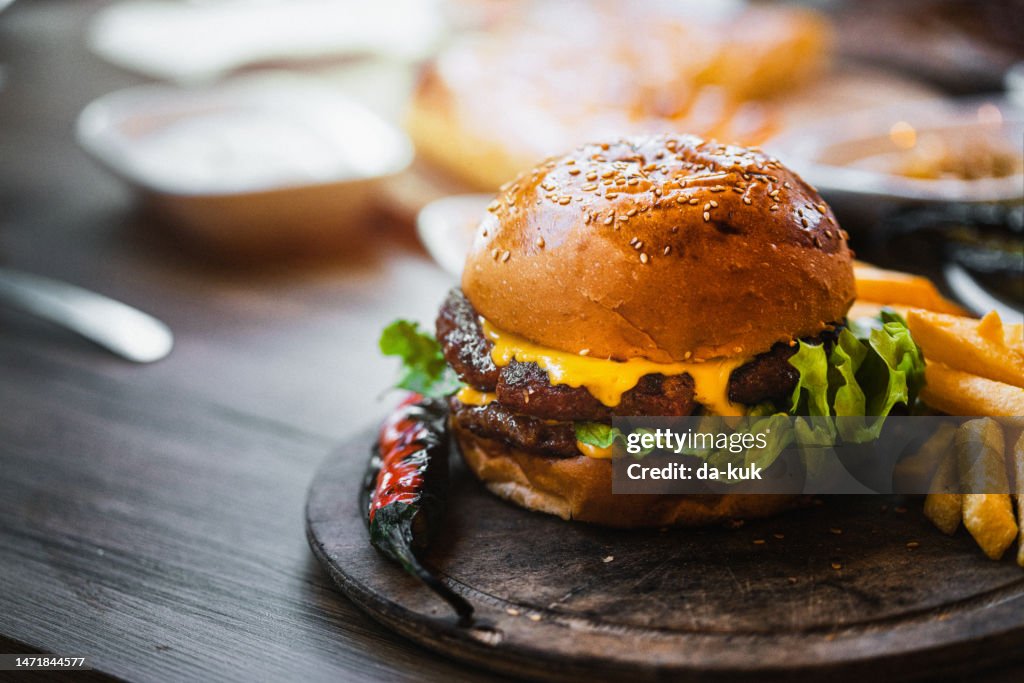 Deliciosa hamburguesa doble con patatas fritas y verduras en tabla de cortar de madera