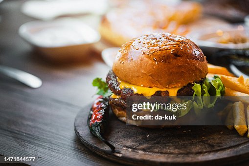 木製まな板にフライドポテトと野菜を添えたおいしいダブルバーガー 木製まな板にフライドポテトと野菜を添えたおいしいダブルバーガー