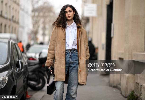 Model Xiomara Cecilia Pupo Pérez is seen wearing a tan jacket, white shirt, blue jeans and black bag outside the Rokh show during Paris Fashion Week...