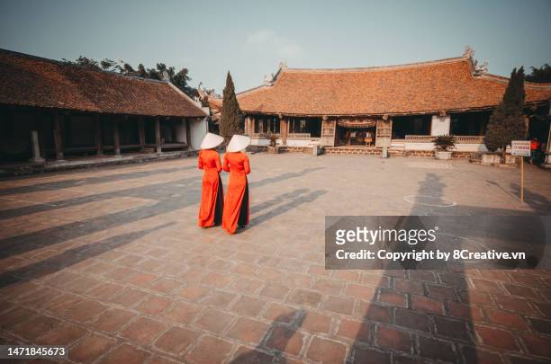 two young lady walking in vietnamese red ao dai dress into temple - tet stock-fotos und bilder