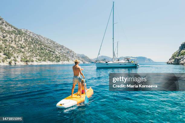 young couple paddling on stand up paddleboards against the yacht in the sea. - türkei stock-fotos und bilder