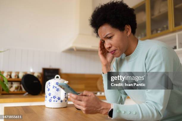 black woman feeling sad while using cell phone at home. - angry on phone stockfoto's en -beelden
