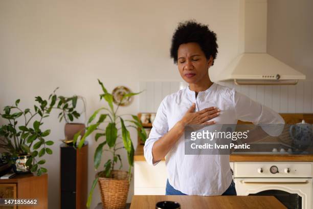 displeased black woman holding her chest in pain at home. - heartburn stock pictures, royalty-free photos & images