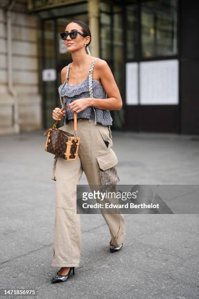 Tamara Kalinic wears black sunglasses, diamonds earrings, a black and white striped print pattern ruffled cropped tank-top with gray checkered...