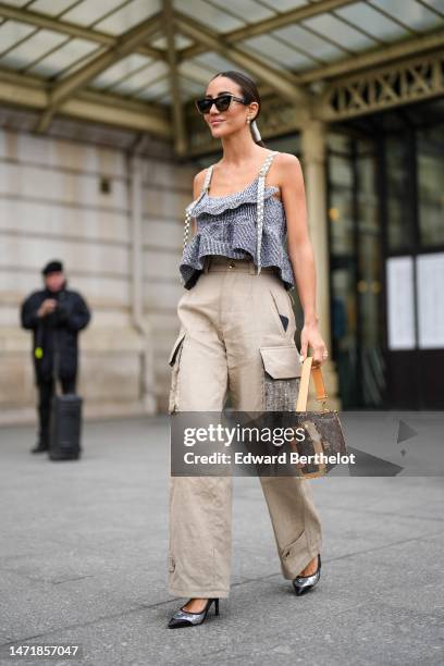 Tamara Kalinic wears black sunglasses, diamonds earrings, a black and white striped print pattern ruffled cropped tank-top with gray checkered...