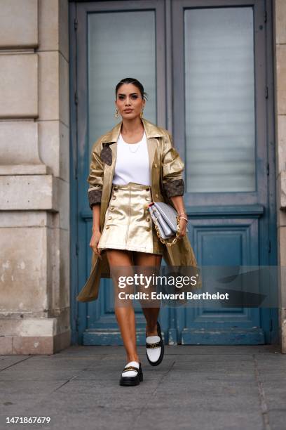 Camila Coelho wears gold logo pendant earrings from Louis Vuitton, a white ribbed tank-top from Louis Vuitton, a gold shiny leather with brown LV...