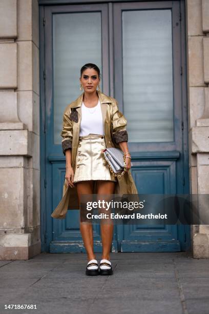 Camila Coelho wears gold logo pendant earrings from Louis Vuitton, a white ribbed tank-top from Louis Vuitton, a gold shiny leather with brown LV...