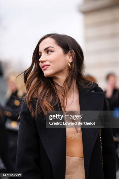 Ana De Armas wears a black wool blazer jacket, a beige and pale orange shiny leather V-neck / short dress, outside Louis Vuitton, during Paris...