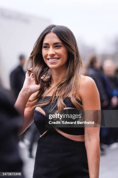 Antonella Roccuzzo wears gold and diamonds earrings, a gold large necklace, a black cut-out pattern / shoulder-off long dress , outside Louis...