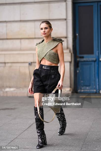 Xenia Adonts wears gold and diamonds earrings, a silver and gold embroidered pattern large straps cropped tank-top from Louis Vuitton, black cargo...