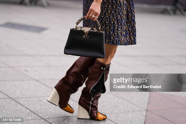 Faye Tsui wears a royal blue / gold / black embossed pattern short skirt from Louis Vuitton, a black shiny leather oversized bomber coat, a black...