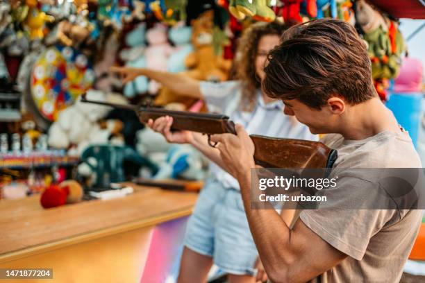 boyfriend shooting a gun at the shooting gallery to win a stuffed animal for his girlfriend - air rifle shooting stock pictures, royalty-free photos & images