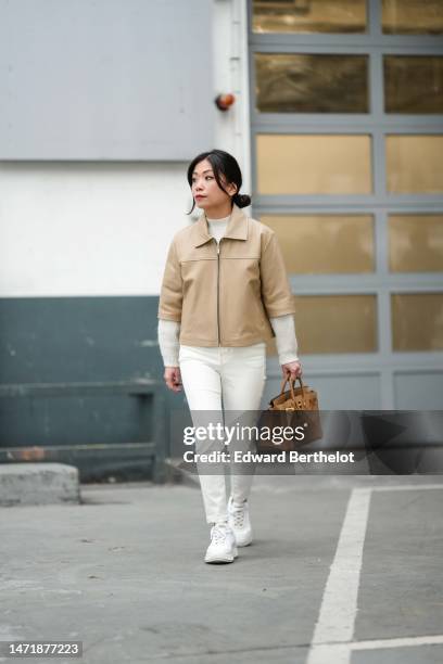 May Berthelot wears a white wool high neck pullover, a beige matte leather zipper short sleeves shirt jacket from Katso, a pale brown Birkin handbag...