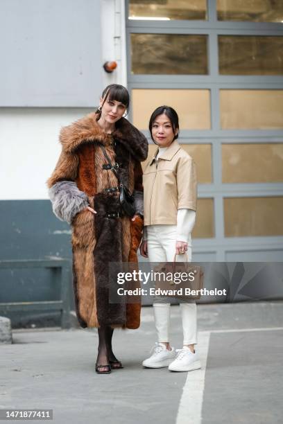 Mary Leest wears black sunglasses, silver earrings, a black t-shirt, a brown / camel / gray embroidered yoke fur long coat, a black shiny leather...