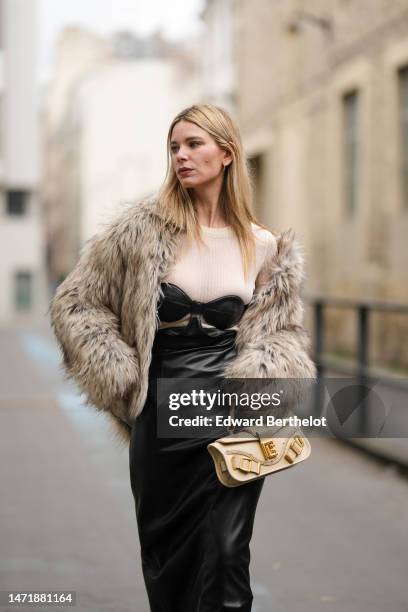 Natalia Verza wears a white latte wool long sleeves t-shirt, a black shiny leather shoulder-off / cut-out waist long dress, a brown gray fur jacket,...