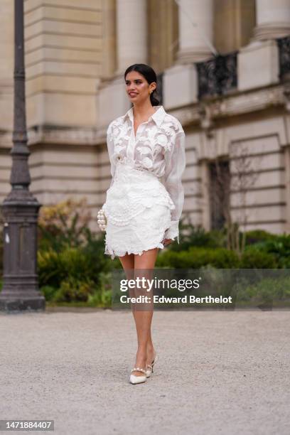 Sara Sampaio wears gold earrings, a white tulle with embroidered pearls and sequined pattern shirt, a matching white pearls and sequined ruffled...