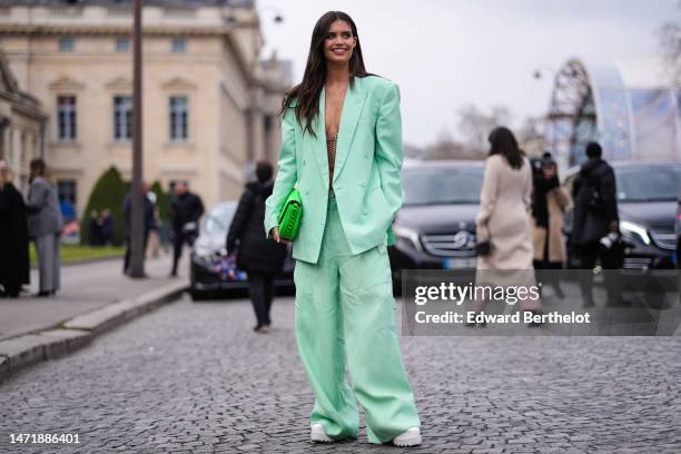 Sara Sampaio wears a pale green oversized blazer jacket, matching pale green wide legs pants, a neon green shiny leather handbag from Stella...