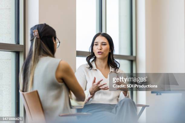 young adult woman gestures and talks during interview with businesswoman - discussie stockfoto's en -beelden
