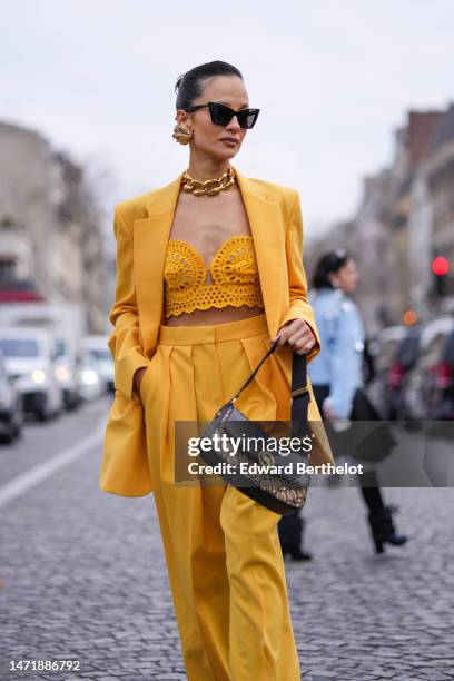 Anna Rosa Vitiello wears gold large earrings, a gold large chain necklace, a yellow cut-out print pattern shoulder-off cropped top, a yellow blazer...