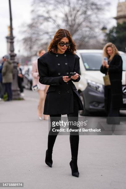 Christine Centenera wears black and camel sunglasses, gold earrings, a black buttoned belted / shoulder-pads jacket, black velvet pointed heels...