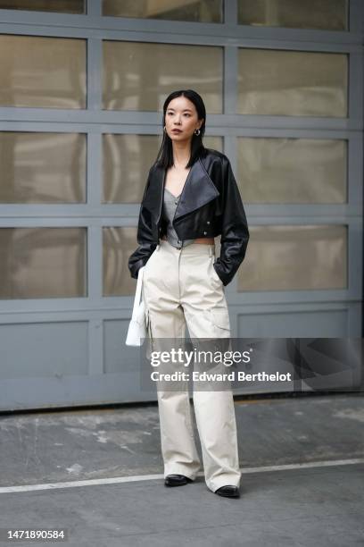 Guest wears silver earrings ,a gray buttoned denim corset tank-top, a black shiny leather cropped jacket, high waist white latte cargo pants, a white...