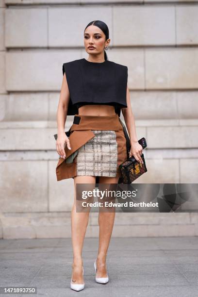 Amina Muaddi wears black and silver rhinestones earrings, a black denim shoulder-pads cropped tank-top from Louis Vuitton, a beige and black...