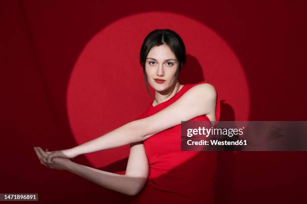 confident young woman posing against red background - classic round one stock pictures, royalty-free photos & images