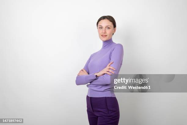 smiling young woman standing with arms crossed over white background - fotografia de três quartos imagens e fotografias de stock