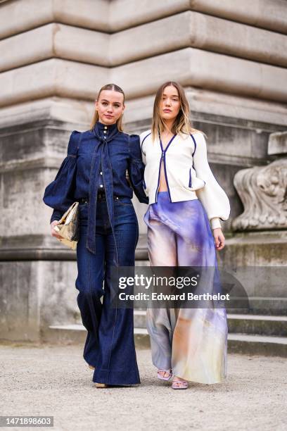 Guest wears gold earrings, a navy blue buttoned high neck denim / long puffy sleeves blouse, matching navy blue denim wide legs pants, a gold shiny...