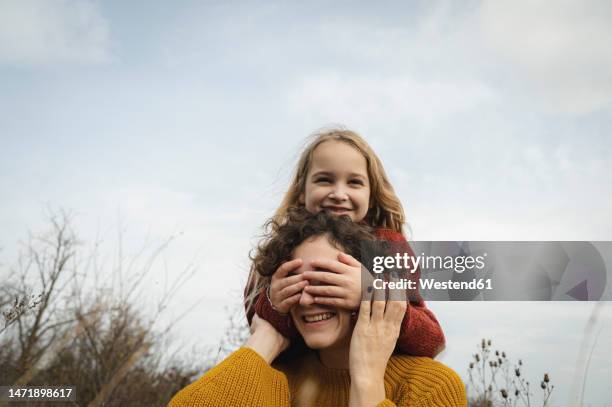 smiling girl covering mother eyes in front of sky - surprised mum stock-fotos und bilder