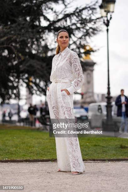 Guest wears gold and diamonds pendant earrings, a white lace print pattern shirt neck / long sleeves / wide legs jumpsuit, a white belt, gold...