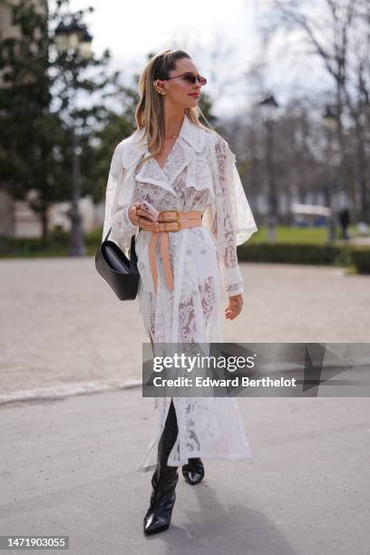 Guest wears burgundy sunglasses, a white lace print pattern cut-out details long dress, a beige shiny leather large belt, a black shiny leather tube...