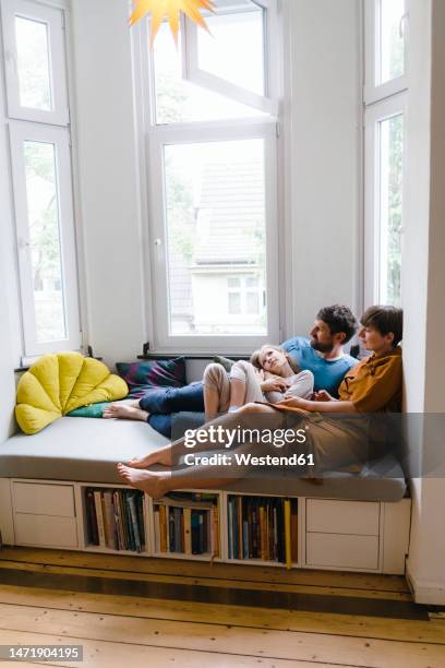 father and mother sitting with daughter on seat at home - window seat stockfoto's en -beelden